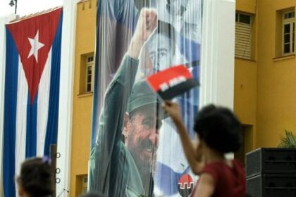Una mujer cubana ondea una bandera cerca de una fotografía de Fidel Castro en el Cuartel Moncada de Santiago de Cuba el 26 de julio de 2008. Se organizaron numerosas festividades en la ciudad para conmemorar el 55 aniversario del asalto al Cuartel Moncada por Fidel Castro.